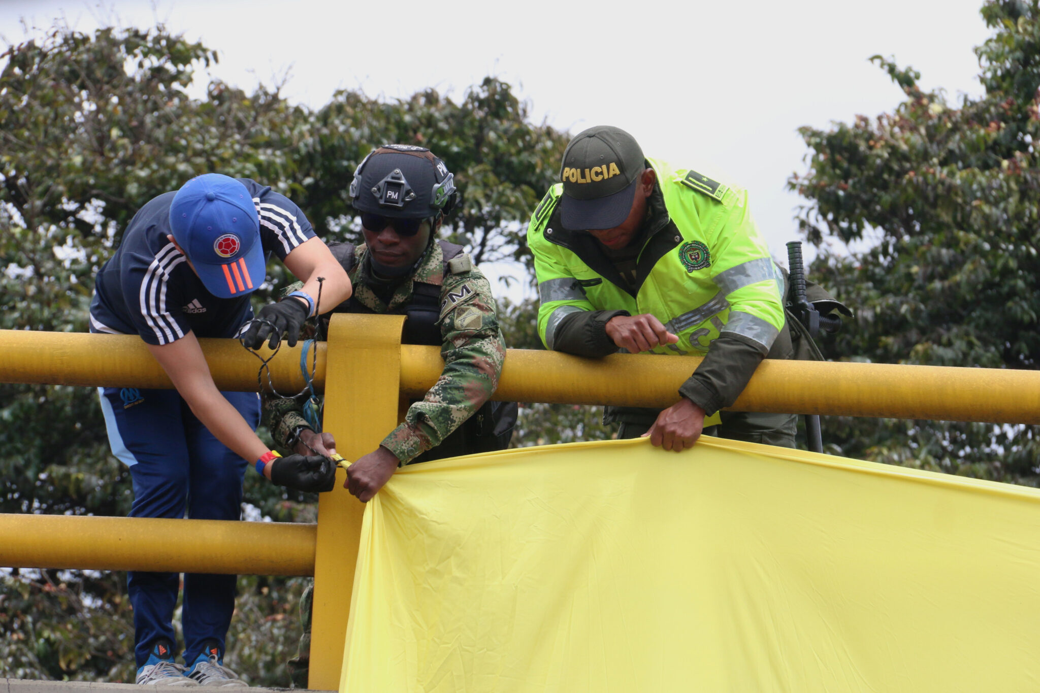 Un civil, un soldado y un policía intentan acomodar una bandera
